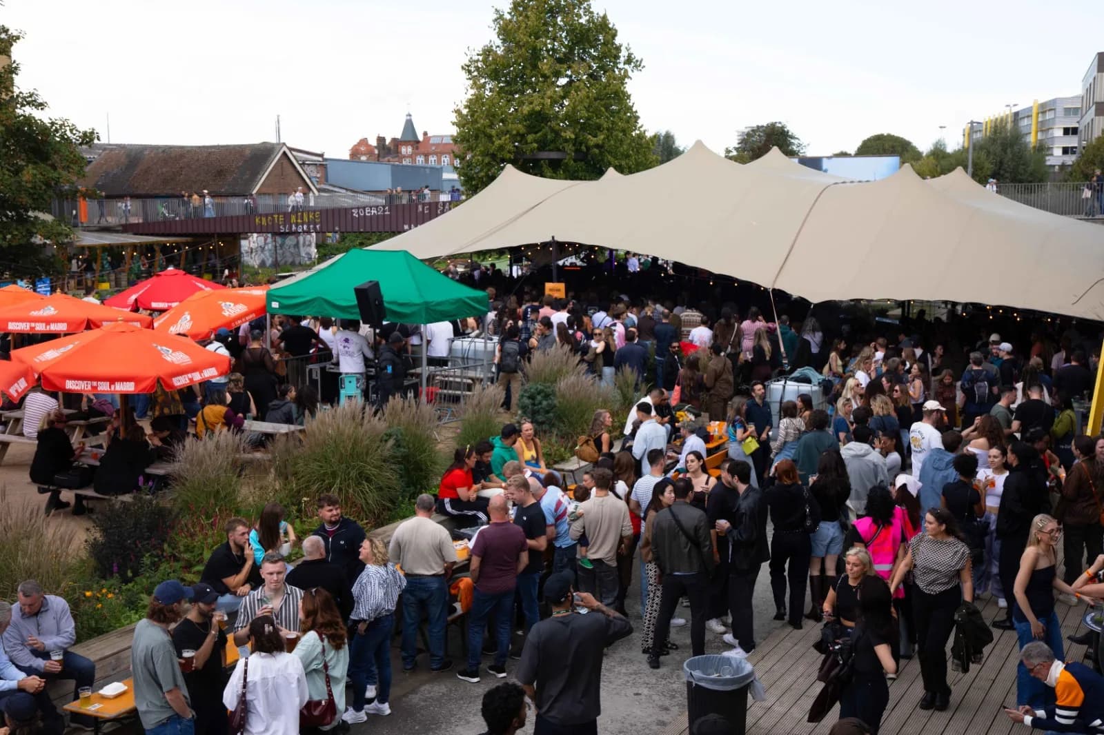 A packed crowd under a marquee and market umbrellas in Hackney Bridge's outdoor Garden space