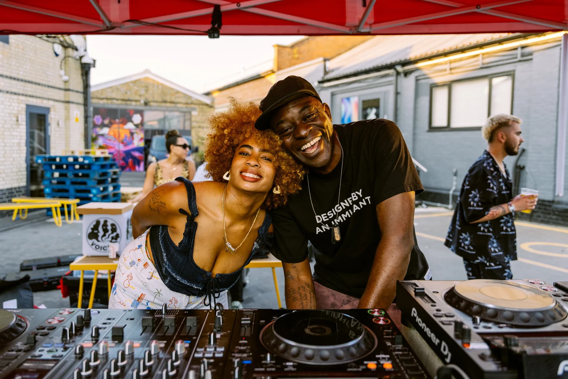 Two DJs sharing a laugh behind the decks at Voices' 2nd birthday party at Two Tribes Campfire